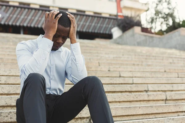 Depressed black businessman with hands on head sitting on stairs