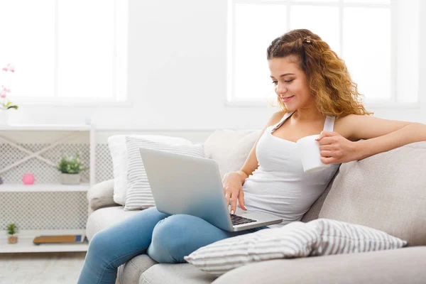 Chica joven con el ordenador portátil sentado en el sofá beige — Foto de Stock