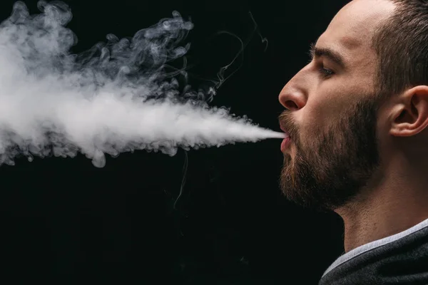 Hombre joven vapeando e-cigarrillo con humo en negro — Foto de Stock