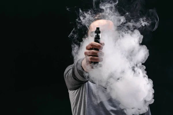 Jeune homme vapotage e-cigarette avec de la fumée sur noir — Photo