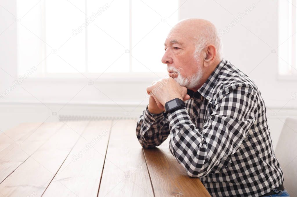 Pensive elderly man sitting at table, copy space