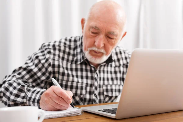 Зрілий чоловік використовує ноутбук і пише в блокноті — стокове фото