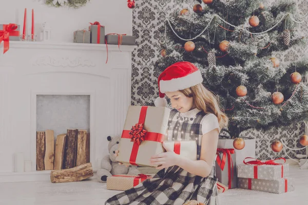 Bella ragazza in cappello di Babbo Natale scartando regali di Natale — Foto Stock