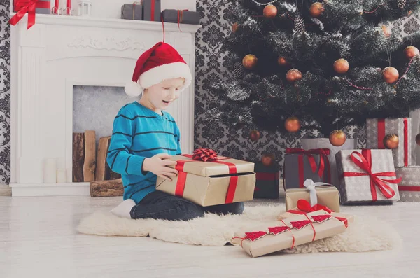 Симпатичний хлопчик у капелюсі Санта, який не завантажує різдвяні подарунки — стокове фото