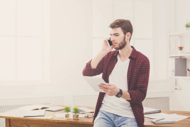 Dijital taplet kullanarak ve cep telefonu Office konuşurken dalgın genç işadamı