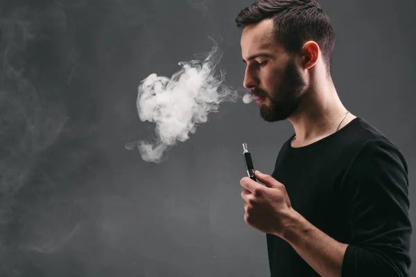 Hombre joven vapeando e-cigarrillo con humo en negro — Foto de Stock