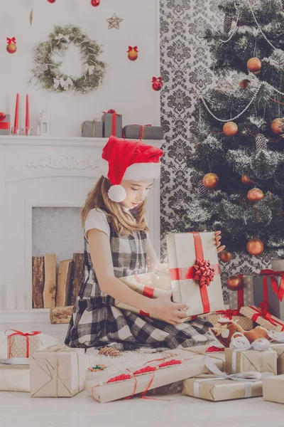 Schönes Mädchen mit Weihnachtsmütze beim Auspacken von Weihnachtsgeschenken — Stockfoto