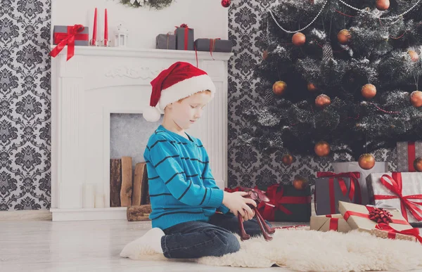 Bonito menino feliz em santa chapéu com presentes de Natal de brinquedo — Fotografia de Stock