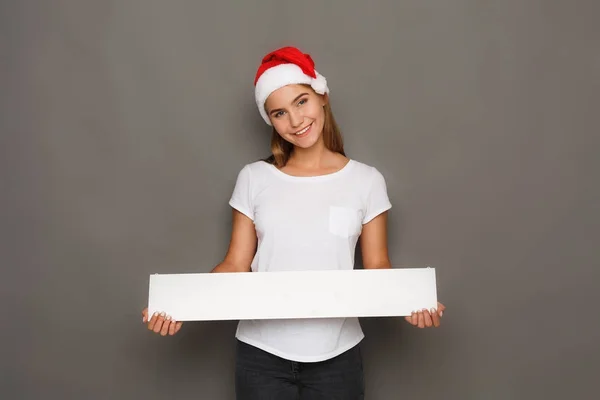 Mladá žena v santa hat drží prázdný bílý nápis — Stock fotografie