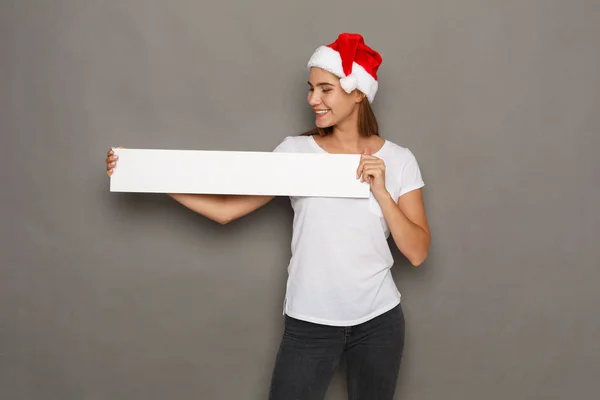 Mladá žena v santa hat drží prázdný bílý nápis — Stock fotografie