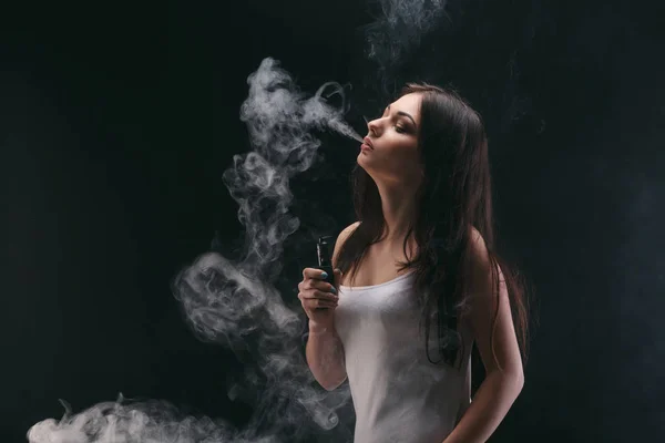 Junge Frau verdampft E-Zigarette mit Rauch auf schwarz — Stockfoto