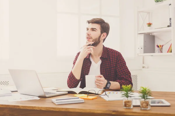 Pensativo joven hombre de negocios con portátil en la oficina blanca moderna — Foto de Stock