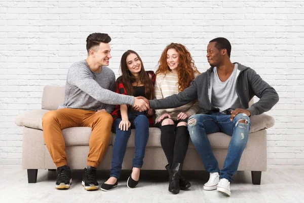 Felices amigos multiétnicos, gente informal sentada en el sofá dentro y riendo — Foto de Stock