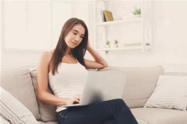 Genç kadınlar beyaz oturma odası kanepe üzerinde oturan dizüstü bilgisayar kullanarak
