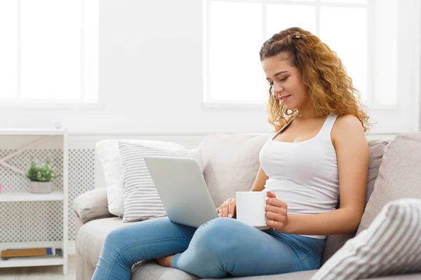 Giovane ragazza con computer portatile seduto sul divano beige — Foto Stock