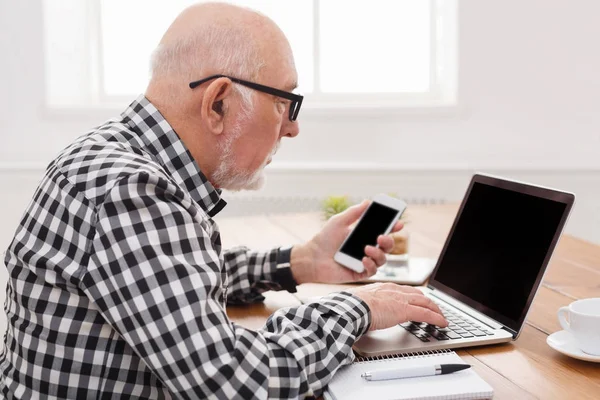 Hombre mayor usando portátil y maqueta de teléfonos inteligentes — Foto de Stock