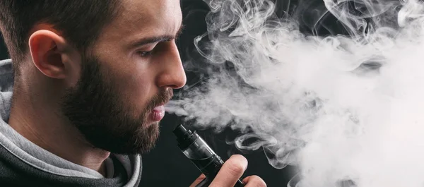 Hombre joven vapeando e-cigarrillo con humo en negro — Foto de Stock