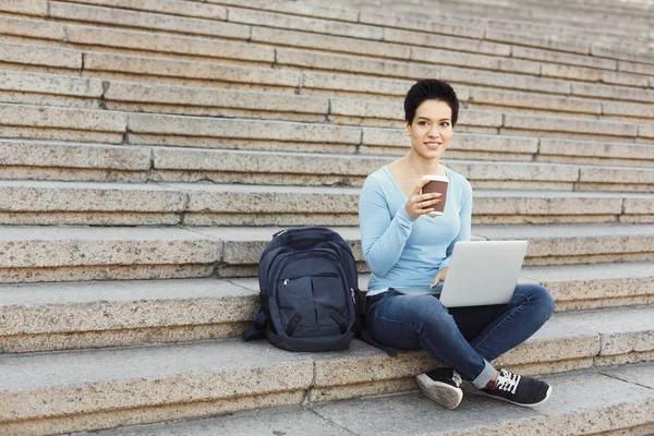 Smilende kvinne sitter i trappen med laptop – stockfoto