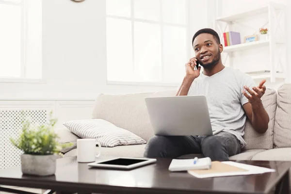 Smiling young man at home with laptop and mobile — Stock Photo, Image