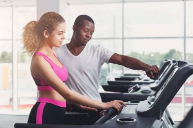Fitness Eğitmeni koşu bandı üzerinde genç kadın yardımcı olur.