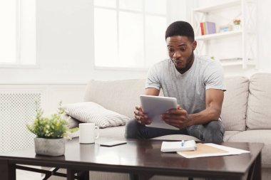 Şaşırmış genç adam evde tablet üzerinde okuma