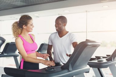 Fitness Eğitmeni koşu bandı üzerinde genç kadın yardımcı olur.