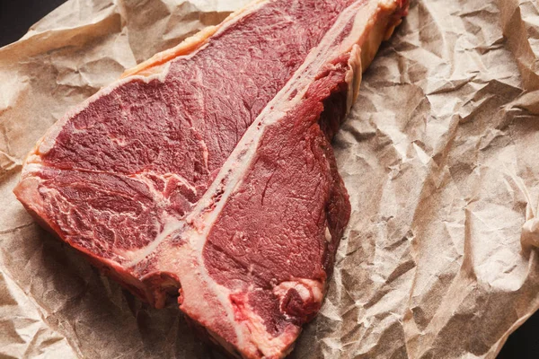 Bistecca di t-bone cruda su papper artigianale su sfondo scuro — Foto Stock