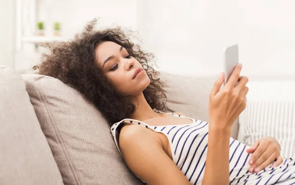 Chica joven usando el teléfono móvil en el sofá —  Fotos de Stock