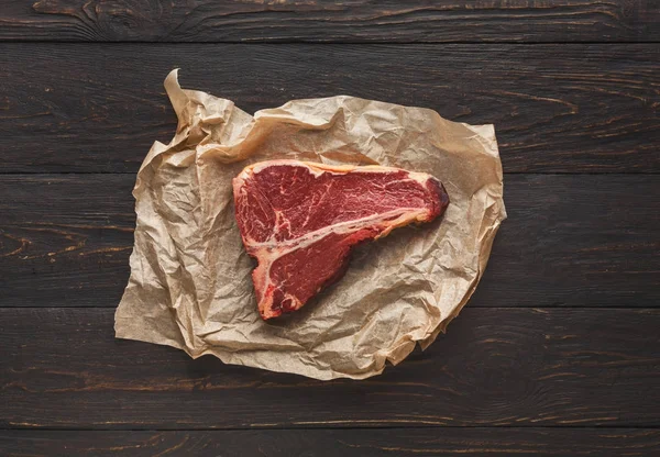 Raw t-bone steak on craft papper on dark background — Stock Photo, Image