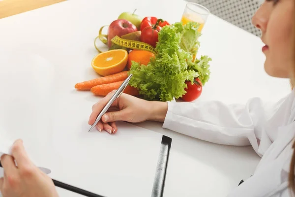 Nutritionist doctor writing diet plan on table — Stock Photo, Image