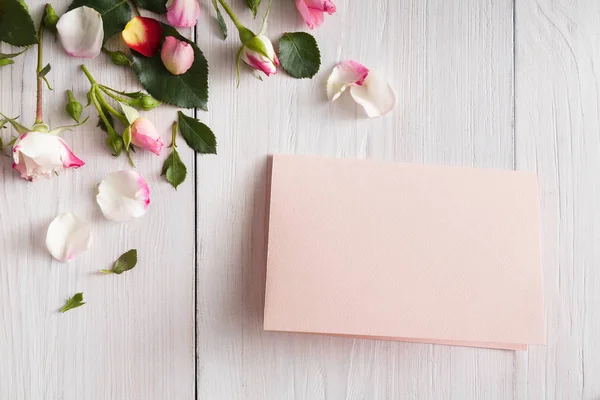 Rosa rosa flores pétalas e cartão de papel artesanal em madeira rústica branca — Fotografia de Stock