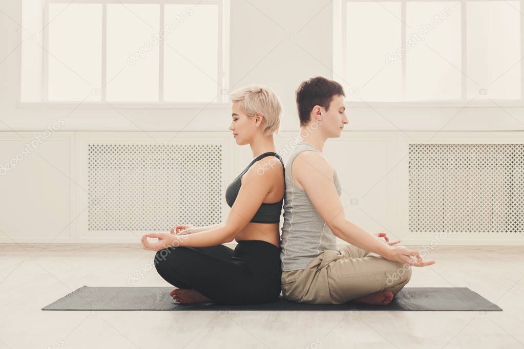 Young couple meditating together, back to back