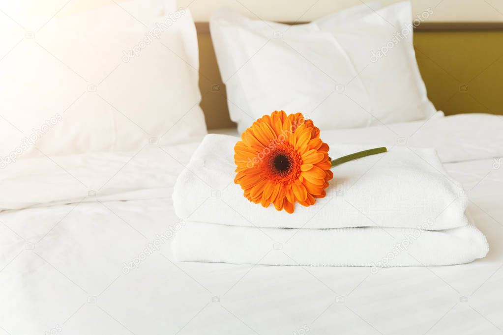 Stack of towels and flower on bed in hotel room