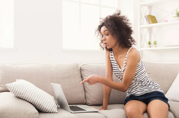Schockiertes Mädchen sitzt mit Laptop auf beigem Sofa — Stockfoto