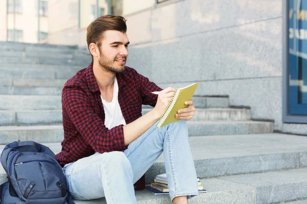 Ung student att göra anteckningar som sitter på trappan — Stockfoto