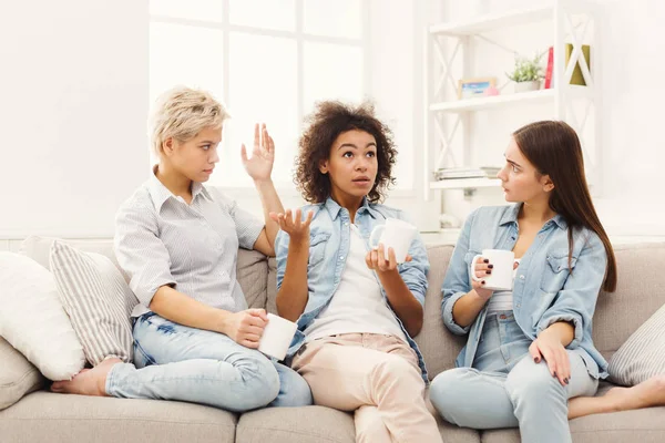 Three young female friends with coffee chatting at home — Stock Photo, Image