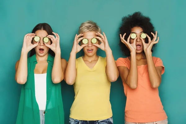 Três meninas bonitas cobrindo os olhos com pedaços de pepino — Fotografia de Stock