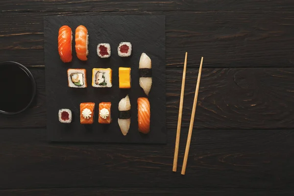 Set of salmon sushi and rolls on black wood background, top view — Stock Photo, Image