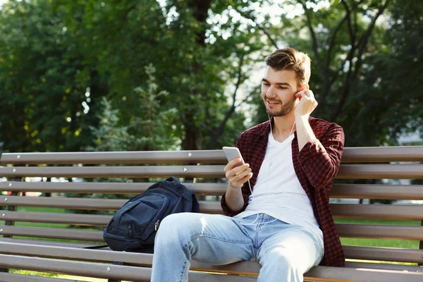 Jovem ouvindo música sentada no parque — Fotografia de Stock