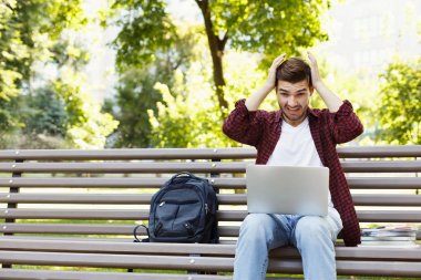 Umutsuz genç adam açık havada dizüstü bilgisayar kullanarak