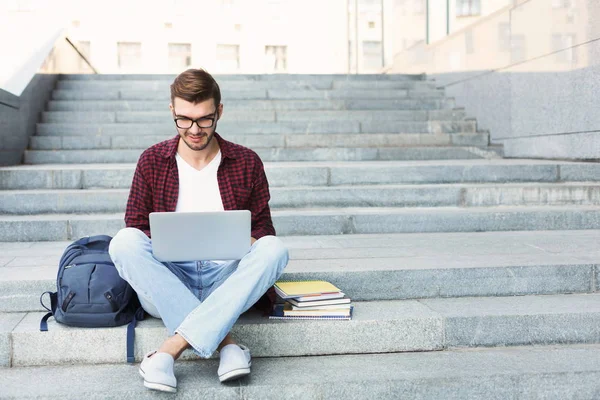 Estudiante sonriente sentado en escaleras usando laptop — Foto de Stock