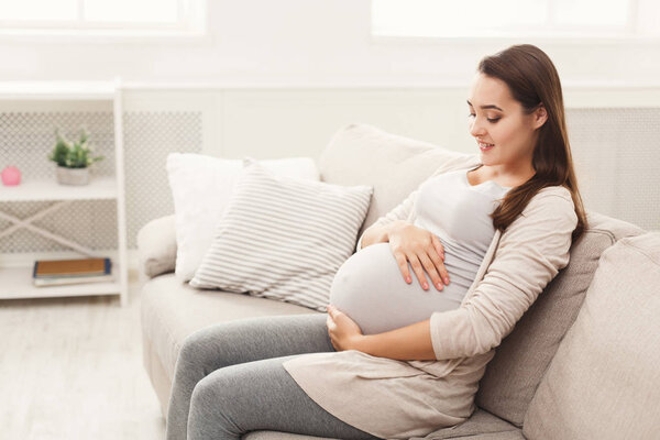 Pregnant woman caressing her belly at home