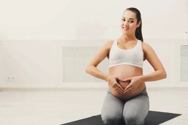 Wanita hamil memegang tangan dalam bentuk hati di perutnya — Stok Foto