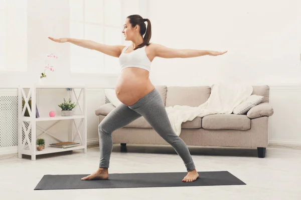 Mujer embarazada feliz entrenamiento yoga en pose de héroe — Foto de Stock