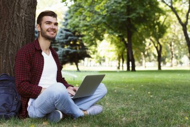 Dizüstü bilgisayar açık havada çim üzerinde oturan adam