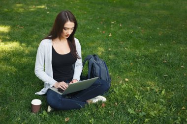 Parkta dizüstü bilgisayar kullanan genç dalgın kadın