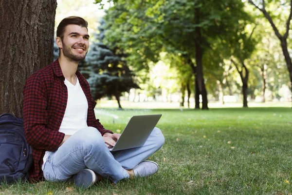 Hombre sentado en la hierba con el ordenador portátil al aire libre — Foto de Stock