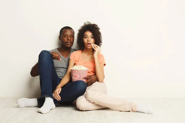 Surprised black couple wathing movie at home on the floor — Stock Photo, Image