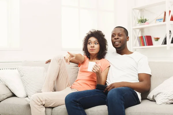 Surpreendido jovem casal afro-americano assistindo TV em casa — Fotografia de Stock