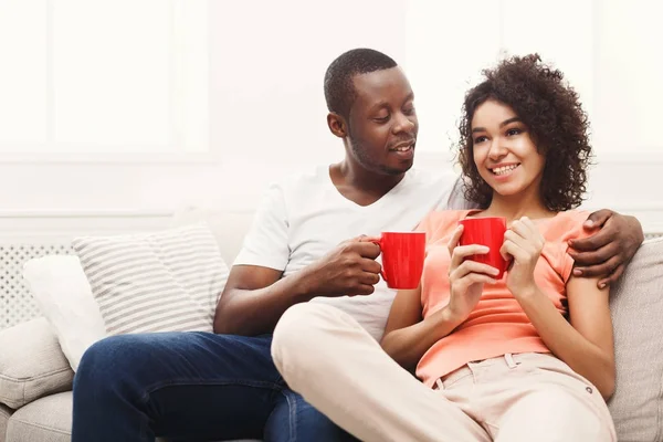 Sonriente pareja negra bebiendo café en el sofá en casa —  Fotos de Stock